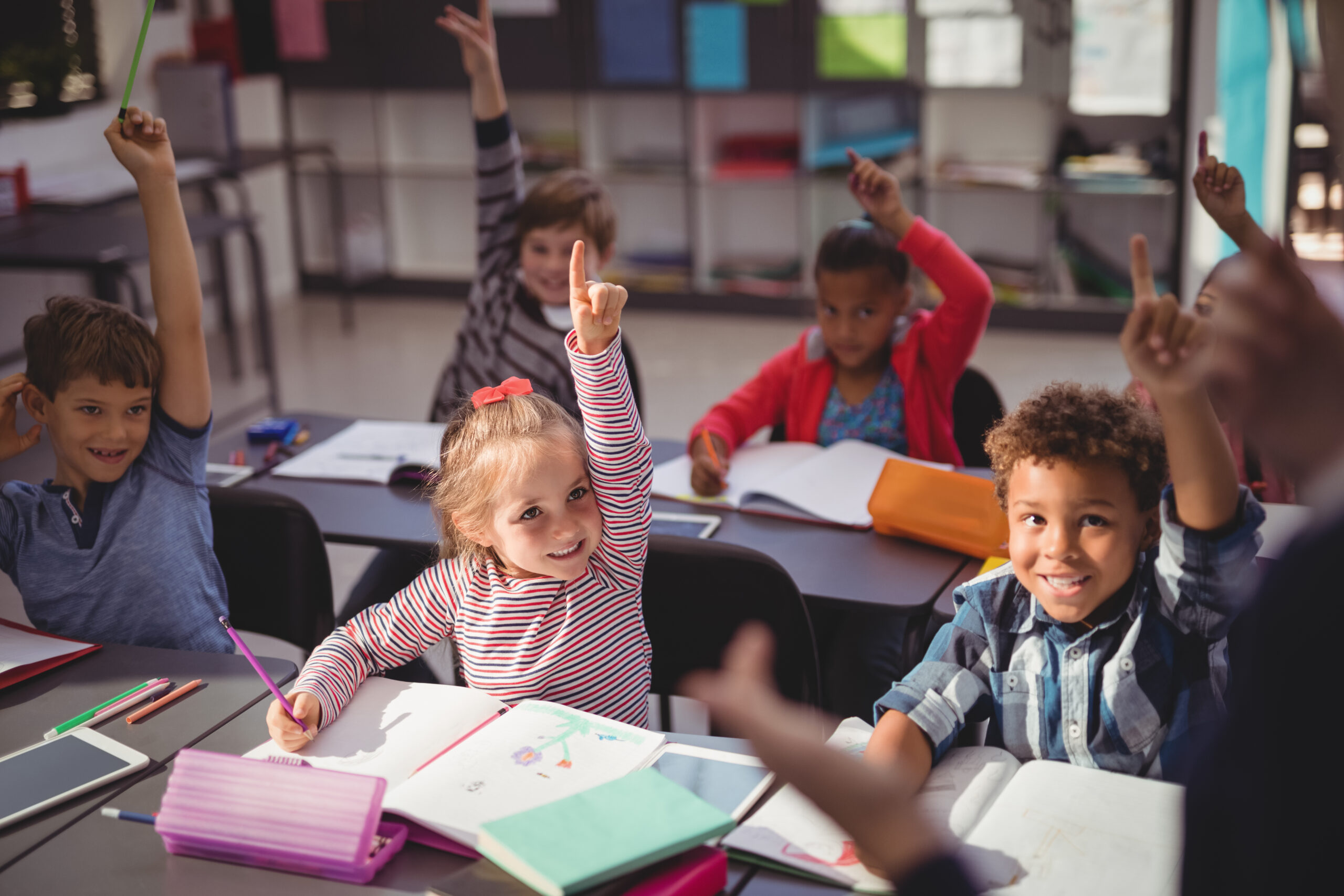 Schoolkids raising their hands in classroom at school